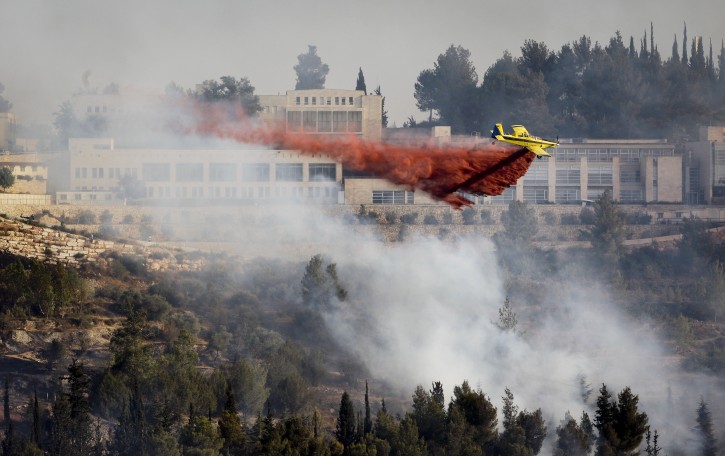 A fire plane drops red fire retardant to try to extinguish fires burning in the forest below Yad Vashem Holocaust memorial, seen in background, in Jerusalem Sunday, July 17, 2011. An out of control wildfire has forced the evacuation of Israel's Holocaust memorial Yad Vashem. (AP Photo/Ben Curtis)