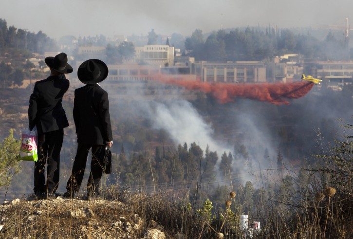 Ultra-Orthodox Jewish boys watch from an opposite hill as a fire plane drops red fire retardant to try to extinguish fires burning in the forest below Yad Vashem Holocaust memorial, seen in background, in Jerusalem Sunday, July 17, 2011. An out of control wildfire has forced the evacuation of Israel's Holocaust memorial Yad Vashem. (AP Photo/Oded Balilty)