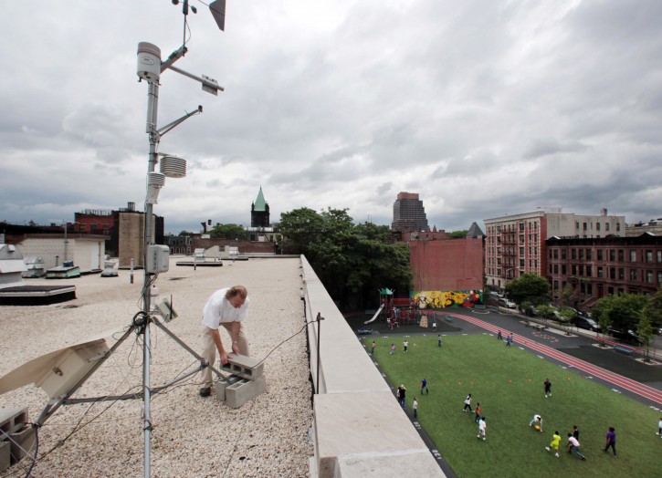 FILE - In this Wednesday, June 24, 2009 file photo, children play on an athletic field below as Wade McGillis, professor of Earth and Environmental Engineering at Columbia University, checks on a rooftop carbon dioxide monitor at an elementary school in the Harlem neighborhood of New York. Putting more green space around an elementary school may help students develop some mental abilities, a study suggests. Green space may help mental development in part by reducing air pollution from vehicles, in addition to helping reduce noise and encouraging physical activity. (AP Photo/Bebeto Matthews, File)