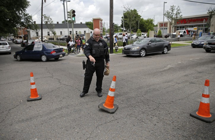 A police officer places cones to divert traffic at the scene where a New Orleans Police officer was shot and killed while transporting a prisoner in New Orleans, Saturday, June 20, 2015. The prisoner remains at large. (AP Photo/Gerald Herbert)