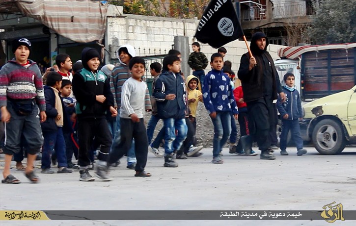 In this photo released on Jan. 14, 2015, by a militant website, which has been verified and is consistent with other AP reporting, Syrian boys, left, follow an Islamic State militant, right, holding his group's flag, during a street preaching session in al-Tabqa in Raqqa province, northeast Syria. IS extremists have made it a priority to mold children under their rule into a new generation of militants, luring them into becoming fighters, suicide bombers and executioners. (Militant website via AP)