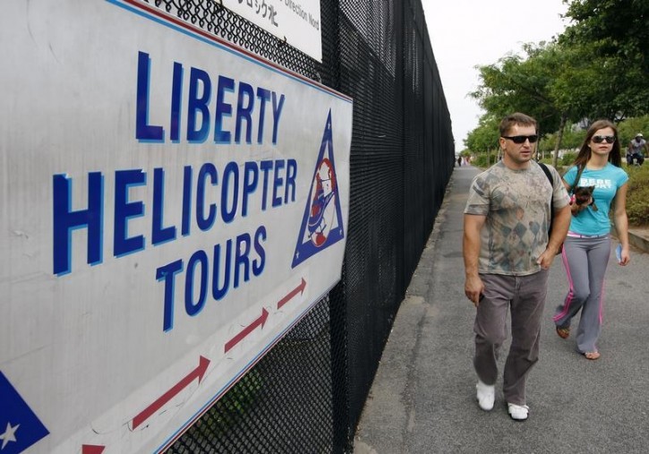 FILE - Two people walk past a sign pointing to the Liberty Helicopter Tours company in New York, August 8, 2009.  Reuters