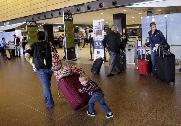 In this March 24, 2015, photo, Colin Drummond, 4, pushes luggage from behind as he walks with family members to check-in a relative for an Alaska Airlines flight at Seattle-Tacoma International Airport in SeaTac, Wash. Fliers in certain markets are seeing bargain flights as fare wars make a limited return. (AP Photo/Elaine Thompson)