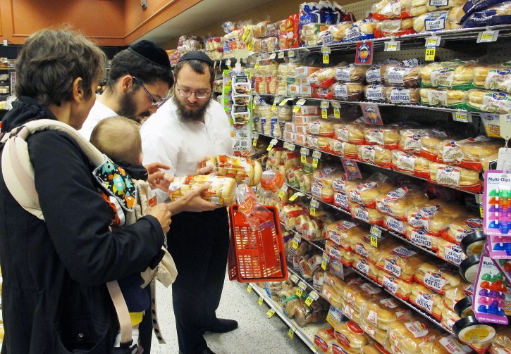 In this July 27, 2015 photo, orthodox Jewish rabbis Dovid Lepkivker, right, and Eli Chaikin, center, inspect packages of bagels with Mary Semple, left, and her grandson Levi Weitner in a grocery store in Helena, Mont. Lepkivker and Chaikin are on a mission to reach as many Montana Jews as they can in a month to teach them how to keep kosher. (AP Photo/Matt Volz)