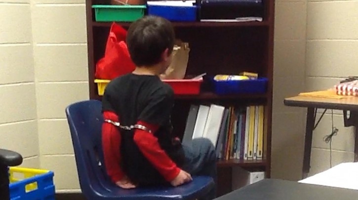 In this image made from video taken in August 2014, and provided by the American Civil Liberties Union on Tuesday, Aug. 4, 2015, an 8-year-old boy struggles and cries out as he sits in a chair with handcuffs around his biceps and his arms locked behind him while a school resource officer stands nearby, at an elementary school in Covington, Ky. The boy’s mother, along with the mother of a 9-year-old girl who was also handcuffed at the school, have filed a federal lawsuit against the school. The lawsuit says both children have attention deficit hyperactivity disorder, and school officials are aware of their disabilities. (American Civil Liberties Union)