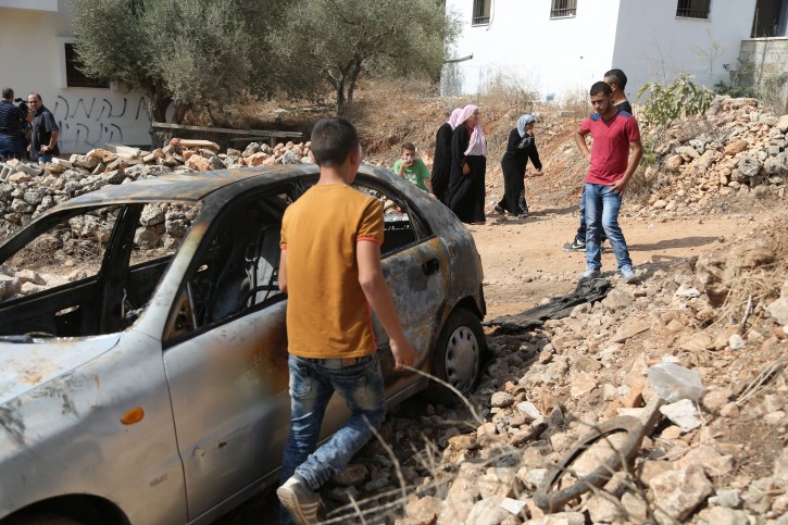 . A Palestinian boy looks at a car belonging to Palestinians, which residents said was burnt by alleged Jewish settlers, in Beit Ilu village near the West Bank city of Ramallah on October 2, 2015. An Israeli couple was murdered last night while driving through the West Bank, an Israeli forces were searching the area for the suspected Palestinian attackers, authorities said. Photo by Flash90