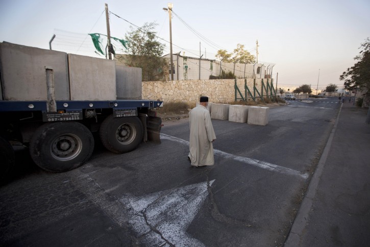 A Palestinian man walks past newly placed concrete blocks on the road at the entrance to the east Jerusalem neighborhood of Jabal Mukaber, Wednesday, Oct. 14, 2015. The Israeli military began deploying hundreds of troops in cities across the country on Wednesday to assist police forces in countering a wave of deadly Palestinian shooting and stabbing attacks that have created panic across the country. (AP Photo/Sebastian Scheiner)
