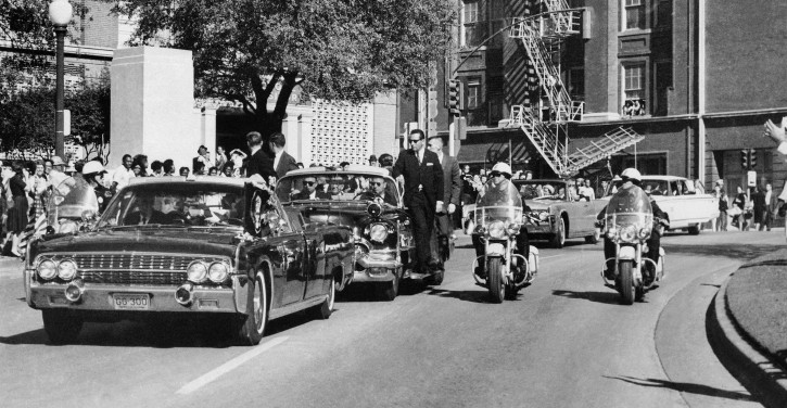 FILE - In this Nov. 22, 1963 file photo, seen through the foreground convertible's windshield, President John F. Kennedy's hand reaches toward his head within seconds of being fatally shot as first lady Jacqueline Kennedy holds his forearm as the motorcade proceeds along Elm Street past the Texas School Book Depository in Dallas. The license plates on the vehicle, which were discarded when the vehicle was sent for upgrades, are going up for auction. (AP Photo/James W. "Ike" Altgens, File)