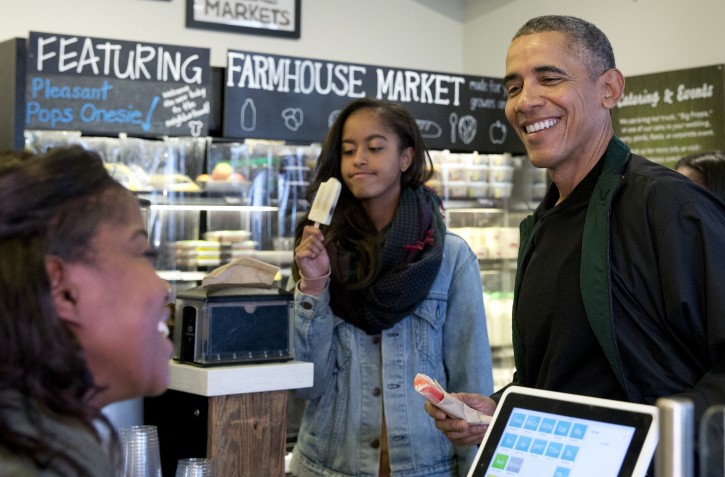 President Barack Obama, joined by his daughters Malia, left, and Sasha, in the background at right, orders a treat at Pleasant Pops on Small Business Saturday in Washington, Saturday, Nov. 28, 2015. (AP Photo/Carolyn Kaster)