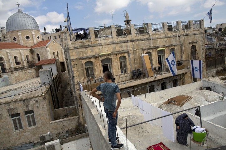 In this Saturday, Oct. 10, 2015 photo, a Palestinian woman takes down laundry on her balcony facing a Jewish seminary in Jerusalem's Old City Muslim Quarters. Under a long-standing U.S. framework for a peace deal, Jerusalem would be divided into two capitals, with Jewish neighborhoods going to Israel and the Arab ones to Palestine. This complex arrangement becomes yet more challenging as more Jews move into Arab areas. (AP Photo/Oded Balilty)