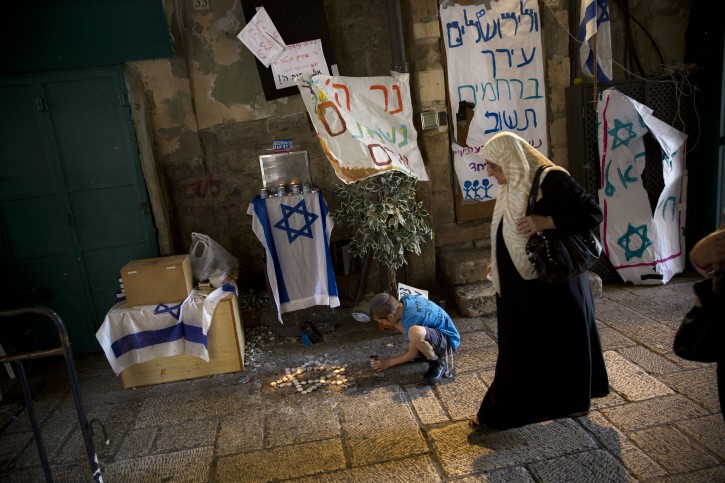 In this Sunday, Oct. 11, 2015 photo, a Palestinian woman walks by Jewish child as he lights candles where a stabbing attack took place last week in Jerusalem's Old City. Under a long-standing U.S. framework for a peace deal, Jerusalem would be divided into two capitals, with Jewish neighborhoods going to Israel and the Arab ones to Palestine. This complex arrangement becomes yet more challenging as more Jews move into Arab areas. (AP Photo/Oded Balilty)