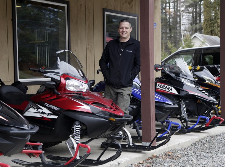 Rick Swift of Village Motorsports, poses with snowmobiles at his business on Tuesday, Dec. 8, 2015, in Speculator, N.Y. Some Northeasterners are beginning to wonder if a white Christmas may just be a dream, and business owners who rely on snow are starting to worry if warm weather could lead to a nightmare winter. (AP Photo/Mike Groll)