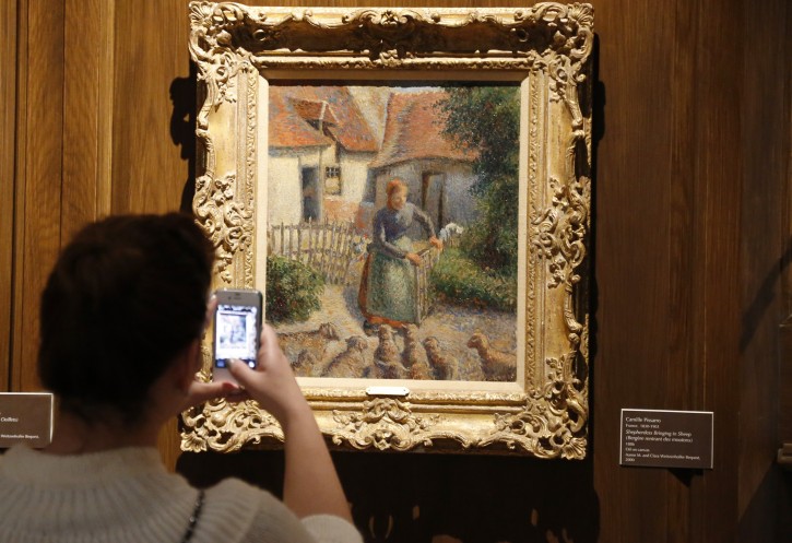FILE - In this Feb. 8, 2014, file photo, a visitor to the Fred Jones Jr. Museum of Art at the University of Oklahoma in Norman, Okla., takes a photograph of a piece called Shepherdess Bringing in Sheep by French impressionist artist Camille Pissarro, at the museum. (AP Photo/Sue Ogrocki, File)