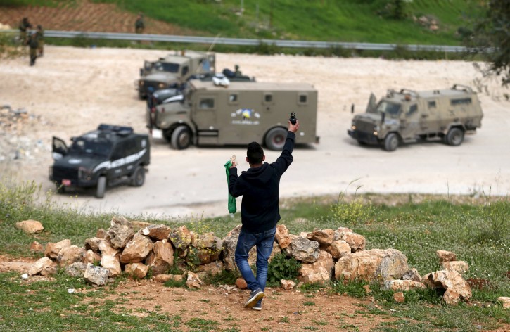 A Palestinian protester holds up an unspent tear gas grenade fired by Israeli troops as he stands in front of the troops during clashes, near Israel's Ofer Prison, near the West Bank city of Ramallah, March 25, 2016. REUTERS/Mohamad Torokman