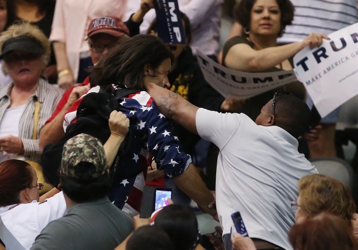 Trump protester Bryan Sanders, center left, is punched by a Trump supporter as he is escorted out of Republican presidential candidate Donald Trump's rally at the Tucson Arena in downtown Tucson, Ariz., Saturday, March 19, 2016. (Mike Christy/Arizona Daily Star via AP) 