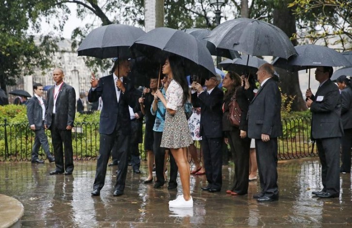 The daughter of U.S. President Barack Obama, Melia (C), stands in the rain as her father talks to a guide as they tour Old Havana, in Havana March 20, 2016. REUTERS/Jonathan Ernst 
