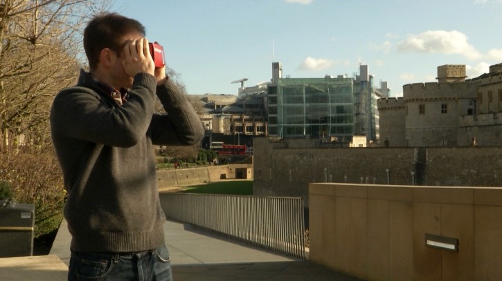 This Feb. 2, 2016 image made from video shows Timelooper co-founder Andrew Feinberg looking through a Google cardboard virtual reality headset across from the Tower of London in London, England. The Timelooper app allows users to experience key moments in London history with just a smartphone and a cardboard headset. (AP Photo)