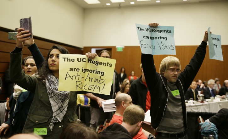 Students hold up protest signs at the end of a public comment period during a University of California Board of Regents meeting Wednesday, March 23, 2016, in San Francisco. AP