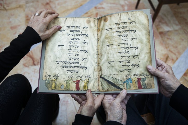 In this photo taken Wednesday, April 13, 2016, Eli and Shuli Barzilai holds a copy of the Birds' Head Haggadah in his house in Jerusalem. Barzilai and his cousins, family grandchildren of one of the earliest Jewish victims of the Nazis are laying claim to a jewel of Israel's leading museum: the world's oldest surviving illustrated Passover manuscript. The descendants of a German Jewish lawmaker say the famed Birds' Head Haggadah, a medieval copy of the text read around Jewish dinner tables on Passover, was stolen from their family during the Nazi era and sold without their consent to the predecessor of the Israel Museum in Jerusalem 70 years ago. (AP Photo/Dan Balilty)