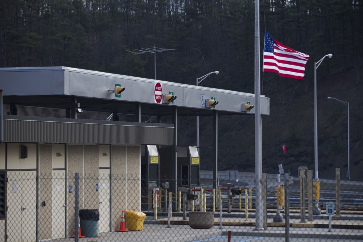 FILE - In a Monday, March 21, 2016 file photo, the Fort Littleton Pennsylvania turnpike exit flies a U.S. flag at half mast after a shooting, in Littleton, Pa.  Martha Berkstresser, a Pennsylvania Turnpike toll collector who survived the botched robbery attempt that left three people dead said she was terrified but her instincts took over during the attack by a retired state trooper, who was killed by police responding to her call for help. (Mark Pynes/PennLive.com via AP, File) 