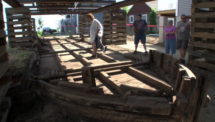 Eileen Scanlon, left, steps across a 44-foot wooden boat on Wednesday, May 25, 2016, underneath a home she rents in Highlands, N.J. The 19th-century boat, likely used to transport coal and other goods, sat undisturbed until workers began raising the home Wednesday to put it on pilings. (Thomas P. Costello/Asbury Park Press via AP)