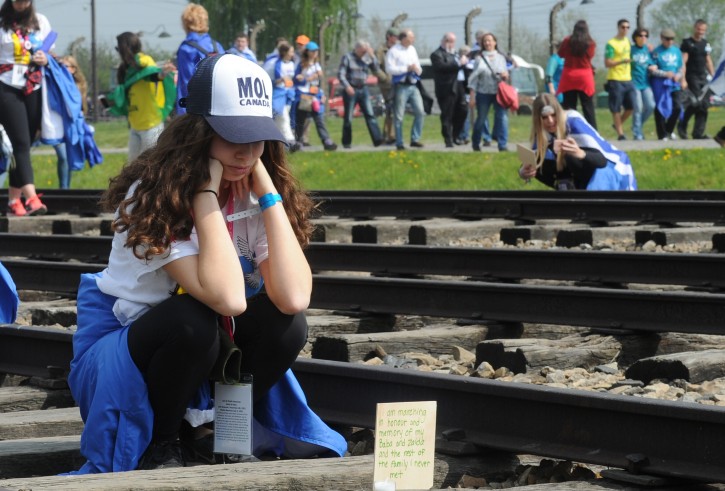 A girl looks at a plaque she just placed on the rail tracks in the former German Nazi Death Camp Auschwitz-Birkenau during the yearly March of the Living, in Brzezinka, Poland, Thursday, May 5, 2016. Thousands of people from around the world have paid homage to the victims of the Holocaust with a somber march from the barracks of Auschwitz to nearby Birkenau. (AP Photo/Alik Keplicz)