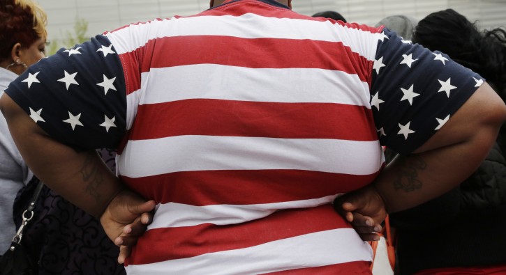 In this Thursday, May 8, 2014 photo, an overweight man wears a shirt patterned after the American flag during a visit to the World Trade Center, in New York. Rising numbers of American adults have the most dangerous kind of obesity, belly fat, despite evidence that overall obesity rates may have plateaued, government data shows. Abdominal obesity affects 54 percent of U.S. adults, versus 46 percent in 1999-2000, and the average waist size crept up an inch, too, according to the most recent statistics. (AP Photo/Mark Lennihan)
