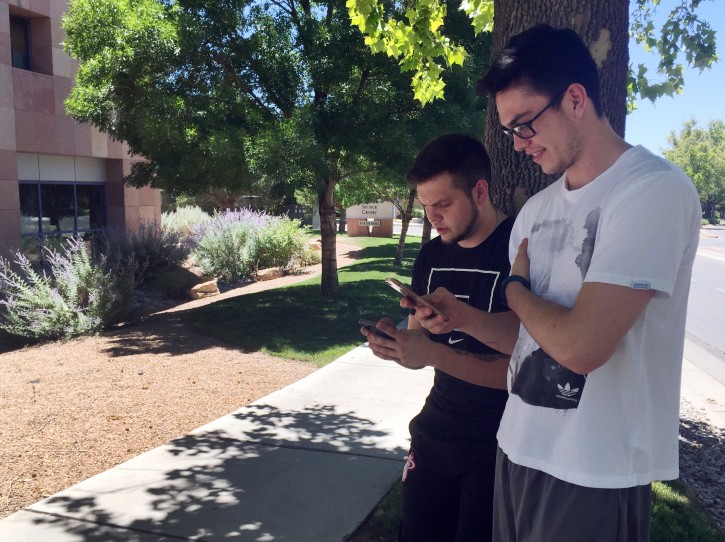Damien Hyatt, 23, left, and his brother, Eron Hyatt, 21, right, walk through an office park in Albuquerque in 93-degree heat on Tuesday, July 12, 2016, while playing "Pokemon Go." Law enforcement agencies nationwide has issued warnings that users playing the "augmented reality" game while roaming through the physical world searching for virtual Pokemon creatures to catch should watch where they are going and avoid going on private property. (AP Photo/Russell Contreras)