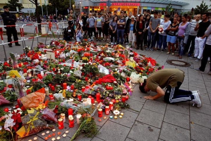 A man prays beside flowers laid in front of the Olympia shopping mall, where yesterday's shooting rampage started, in Munich, Germany July 23, 2016. REUTERS/Arnd Wiegmann