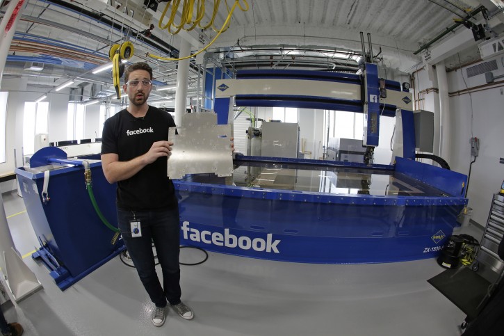 In this photo taken Tuesday, Aug. 2, 2016, model maker Spencer Burns, holds up a piece of sheet metal while standing in front of a water jet during a tour of Area 404, the hardware R&D lab, at Facebook headquarters in Menlo Park, Calif. (AP Photo/Eric Risberg)