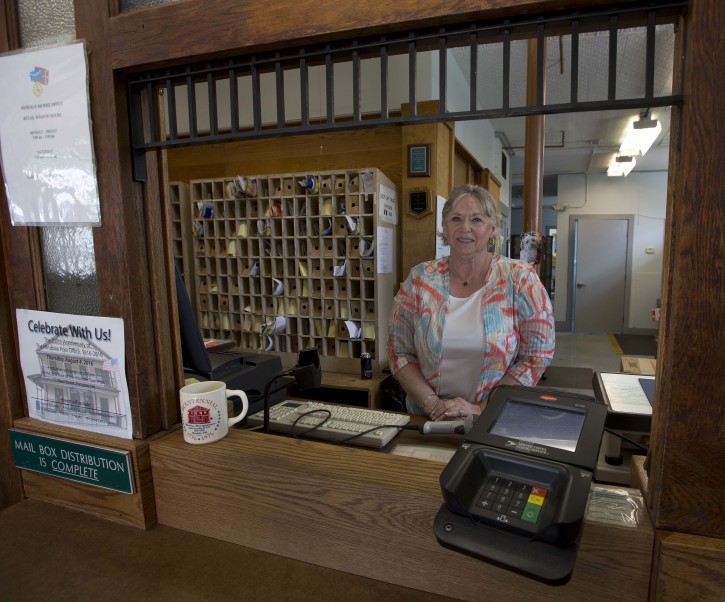 Postmaster Cindy Mason poses behind the window at the oldest continuously operating post office in the U.S., the Hinsdale Post Office in Hinsdale, New Hampshire,Thursday Aug. 4, 2016. The post office is celebrating its 200th birthday. (AP Photo/Jim Cole)