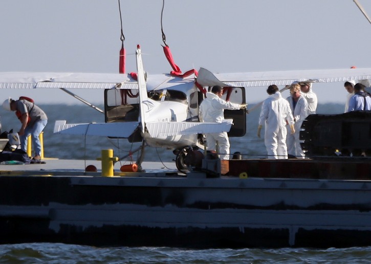 Investigators look over a small plane that was lifted by a crane from the water of Lake Pontchartrain onto a barge near Lakefront Airport, Tuesday, Aug. 30, 2016 in New Orleans. New Orleans Fire Department spokesman Gregory Davis said the bodies of the pilot and a passenger were in the plane's cabin. A second passenger, a woman, survived Saturday night's crash when she was picked up a boat in the area. (Michael DeMocker/NOLA.com The Times-Picayune via AP)