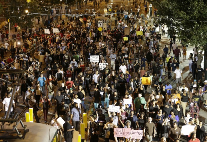 Demonstrators protest Tuesday's fatal police shooting of Keith Lamont Scott in Charlotte, N.C. on Wednesday, Sept. 21, 2016. Protesters rushed police in riot gear at a downtown Charlotte hotel and officers have fired tear gas to disperse the crowd. At least one person was injured in the confrontation, though it wasn't immediately clear how. Firefighters rushed in to pull the man to a waiting ambulance. (AP Photo/Chuck Burton)