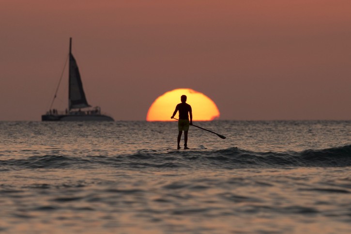 FILE - In this Tuesday, Dec. 31, 2013, file photo, a paddleboarder looks our over the Pacific Ocean as the sun sets off of Waikiki Beach, in Honolulu. Airline mileage cards usually arenât the best way to earn a free vacation. For most fliers, a cash back credit card could be the most rewarding path. (AP Photo/Carolyn Kaster, File)