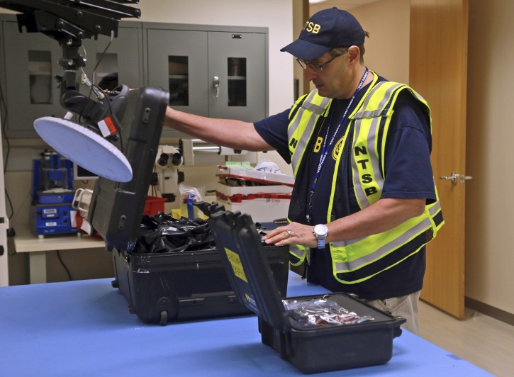 In this photo released by the National Transportation Safety Board (NTSB), National Transportation Safety Board engineer William Tuccio removes the event recorder memory board and video recorder hard drive, recovered from N.J. Transitâs Pascack Valley Line train No. 1614 lead car, from protective cases after the items arrived at an NTSB laboratory, Tuesday, Oct. 4, 2016, in Washington.  Federal investigators recovered a data recorder, video recorder and the engineer's cellphone Tuesday from the commuter train that crashed into a New Jersey rail station last week. The items arrived at the lab for analysis. (Chris OâNeil/NTSB via AP)
