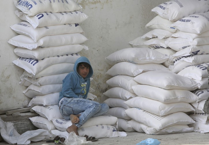 A refugee sits on sacks of flour while he waits to receive food aid from UN food distribution center in Nusseirat refugee camp, central Gaza Strip, Wednesday, Jan. 17, 2018.  (AP Photo/Adel Hana)