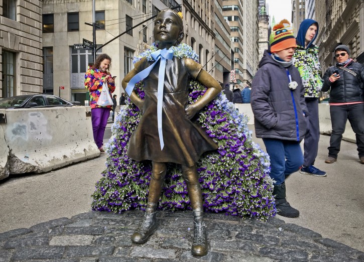 Wall Street's "Fearless Girl" statue is draped with a bouquet of flowers to mark International Women's Day, Thursday March 8, 2018, in New York.  A year ago in the cover of night, an investment firm placed the bronze girl with the defiance stance near the iconic Wall Street Bull statue, drawing attention to workplace gender issues.  (AP Photo/Karen Matthews)