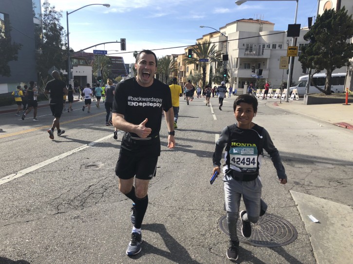 In this March 18, 2018, photo provided by Pash Pashkow, movie production lawyer Loren Zitomersky, left, runs the Los Angeles Marathon backward as a young runner briefly accompanies him. Zitomersky, 33, has embarked on a singular, if odd, quest: At next monthÃ¢ÂÂs Boston Marathon, heÃ¢ÂÂll attempt to break the world record for running the distance backward. Known on social media as Ã¢ÂÂBackwards Guy,Ã¢ÂÂ Zitomersky is trying to raise money and awareness for a cure for epilepsy, which killed a brother he never had a chance to meet. (Pash Pashkow via AP)
