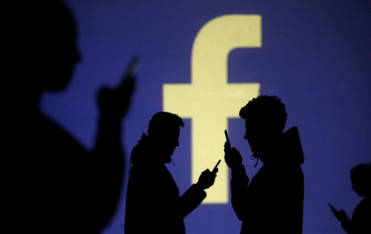 Silhouettes of mobile users are seen next to a screen projection of Facebook logo in this picture illustration taken March 28, 2018.  REUTERS/Dado Ruvic/Illustration