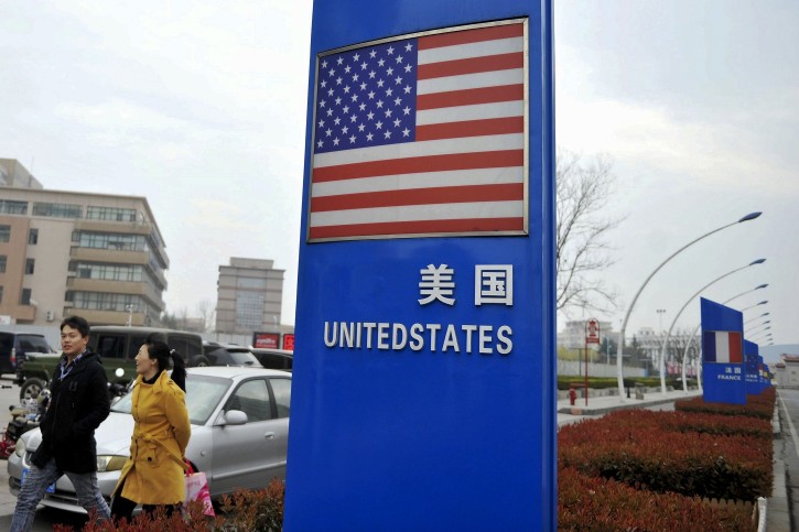 In this Thursday, April 5, 2018 photo, a couple walk by an American flag signboard on display outside a supermarket selling imported groceries at the Qingdao bonded zone in east China's Shandong province. AP