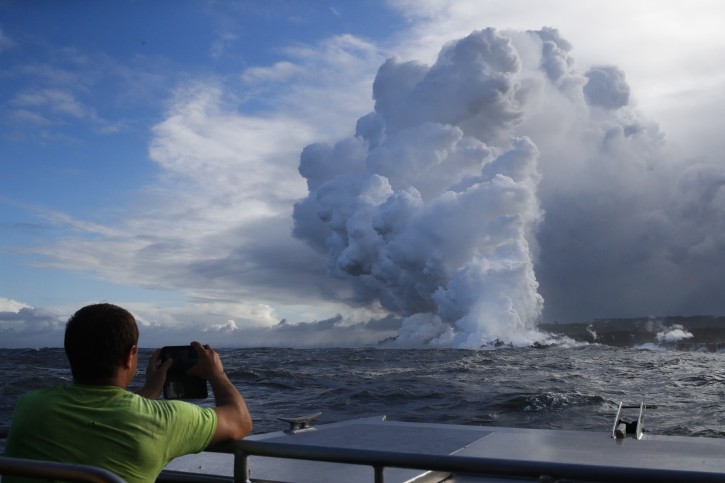 FILE - In this May 20, 2018 file photo, Joe Kekedi takes pictures as lava enters the ocean, generating plumes of steam near Pahoa, Hawaii.  (AP Photo/Jae C. Hong, File)