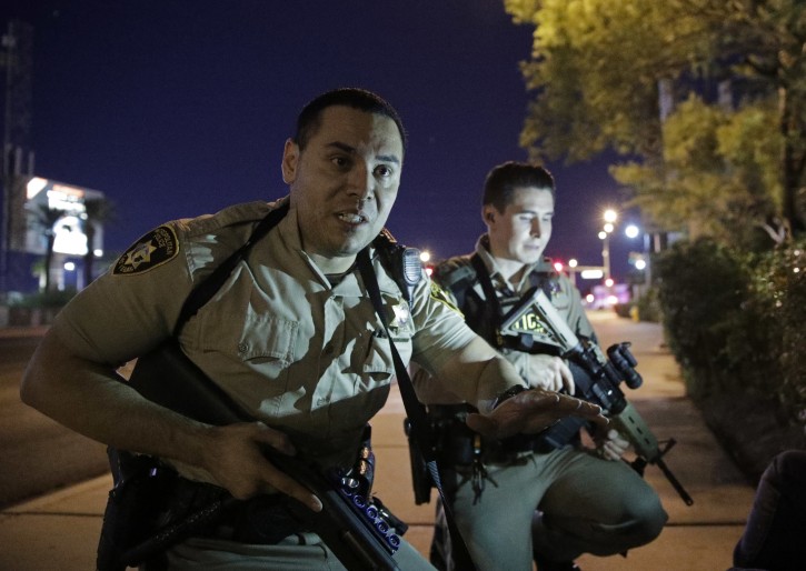 FILE - In this Oct. 1, 2017, file photo, police officers advise people to take cover near the scene of a shooting near the Mandalay Bay resort and casino on the Las Vegas Strip in Las Vegas. A veteran police officer's self-described freeze in a Las Vegas hotel hallway while a gunman fired on an outdoor concert crowd is prompting a review of whether lives could have been saved if officers had acted faster to stop the mass shooting. (AP Photo/John Locher, File)