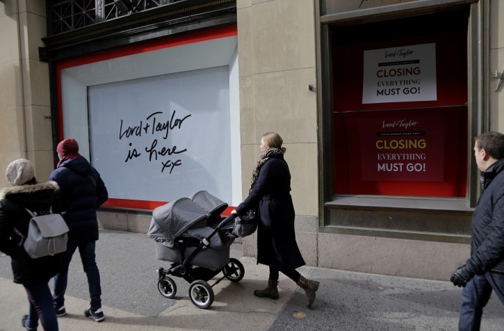 In this Nov. 20, 2018 photo, pedestrians pass by the undercoated windows in the front of Lord & Taylor in New York. Lord & Taylor was the city's first department store to turn its big sidewalk windows into animated, theatrical holiday displays, but its parent company plans to close the Fifth Avenue store in January 2019, after one last blowout sale. (AP Photo/Seth Wenig)