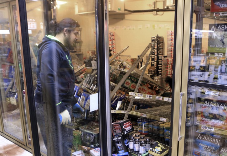 Aisoli Lealasola prepares to clean up fallen cases of beer in a cooler at a liquor store, Value Liquor, after an earthquake on Friday, Nov. 30, 2018, in Anchorage, Alaska. Owner Mary Funner says beer, wine and other bottled alcohol was strewn throughout store aisles after the quake. She considered closing Friday until customers began lining up. They were allowed to come in in small groups. "We're still in business, but we're only open only a little bit at a time," she said. (AP Photo/Dan Joling)
