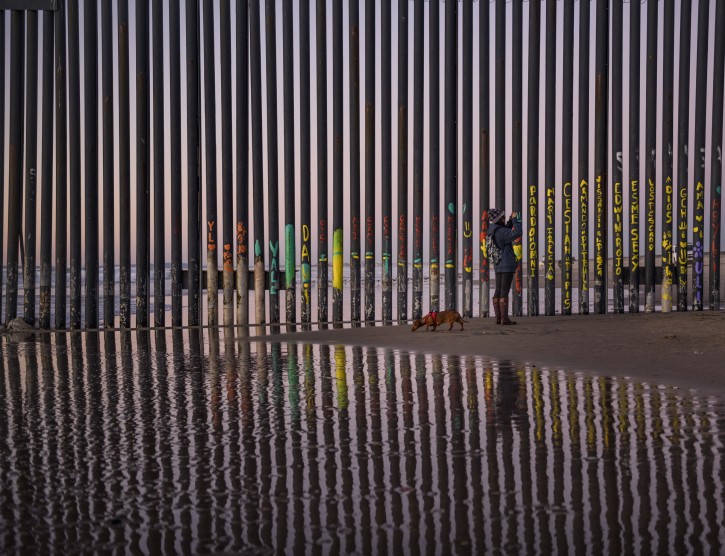 A woman takes a snapshot by the border fence between San Diego, Calif., and Tijuana, as seen from Mexico, Thursday, Jan. 3, 2019. Discouraged by the long wait to apply for asylum through official ports of entry, many migrants from recent caravans are choosing to cross the U.S. border wall and hand themselves in to border patrol agents. (AP Photo/Daniel Ochoa de Olza)