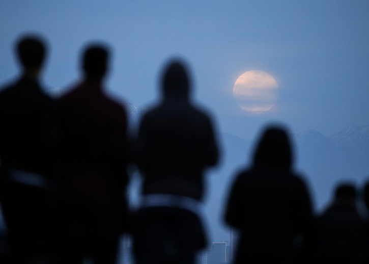 People watch the 'Super Moon' rises behind downtown Los Angeles skyline, from Kenneth Hanh Park in Los Angeles, Sunday Jan. 20, 2019. (AP Photo/Ringo H.W. Chiu)
