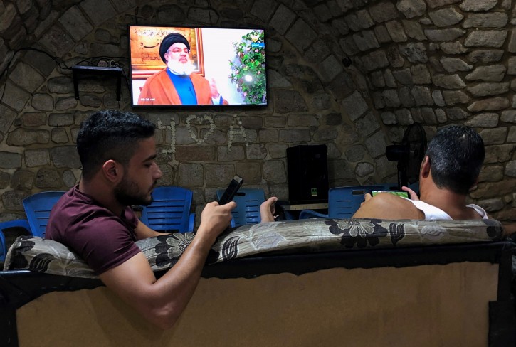 Men hold their phones as they watch Lebanon's Hezbollah leader Sayyed Hassan Nasrallah speak on television inside a coffee shop in the port city of Sidon, Lebanon July 12, 2019. REUTERS/Ali Hashisho